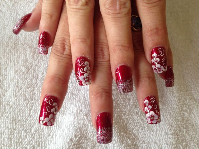 Deep red acrylic nails with silver glitter tips and hand-painted white flowers