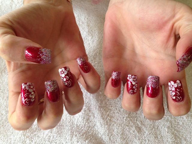 Red nails with glitter tips and white flower art, both hands